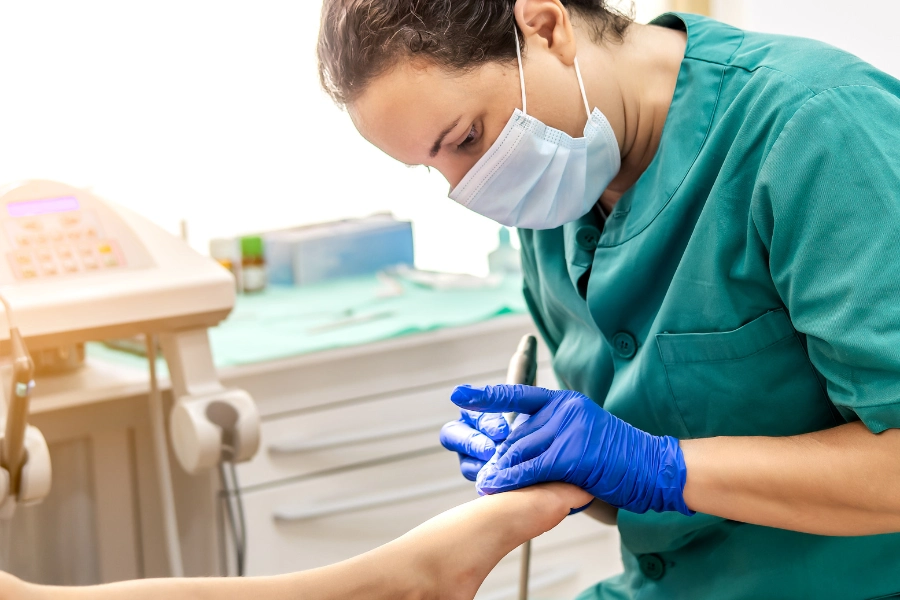 Masked podiatrist in blue gloves examining patient's foot to illustrate a career in podiatry professional setting