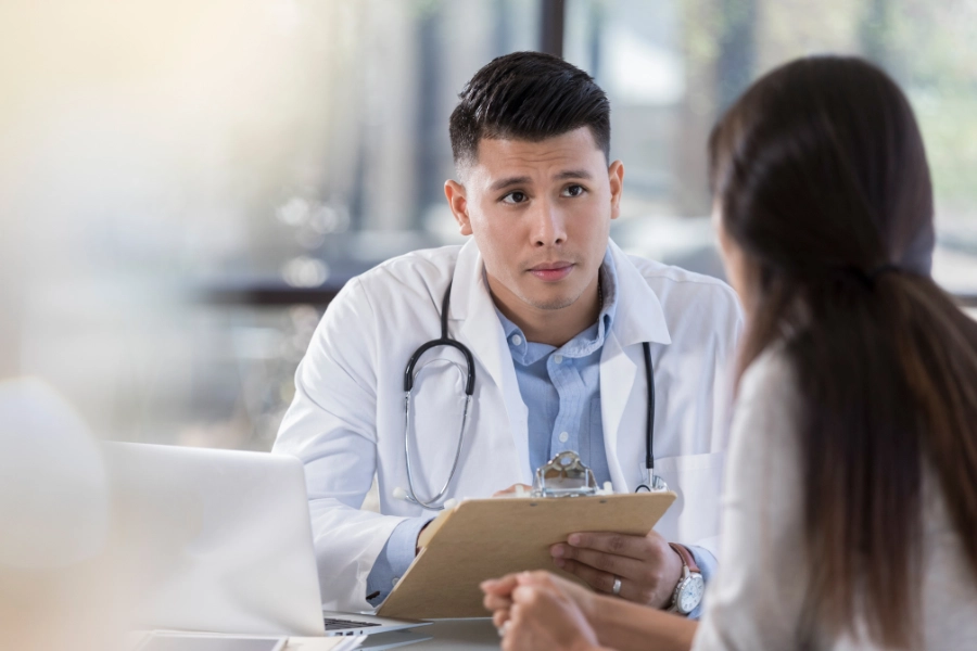 Male podiatrist in scrubs holding a clipboard while talking to a patient about podiatry care and Cigna insurance coverage