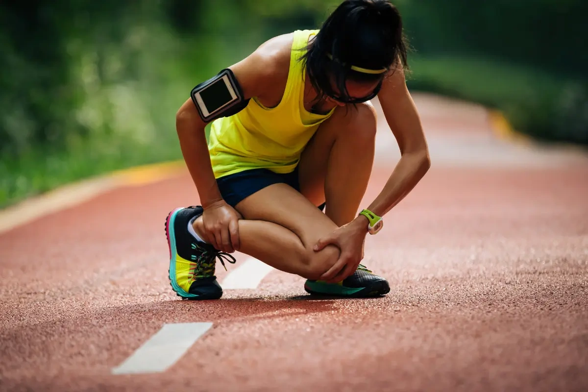 Female runner in yellow kneeling on track holding knee in pain