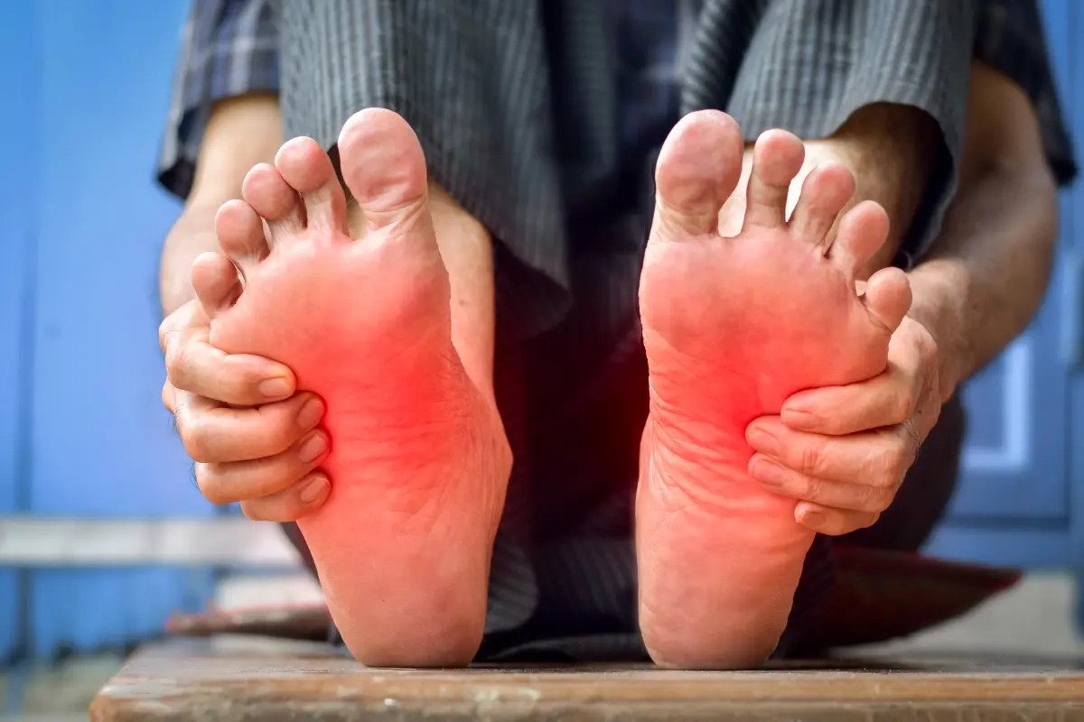 Man holding red, achy feet in pain, showing symptoms of nerve damage, burning, and tingling in the foot