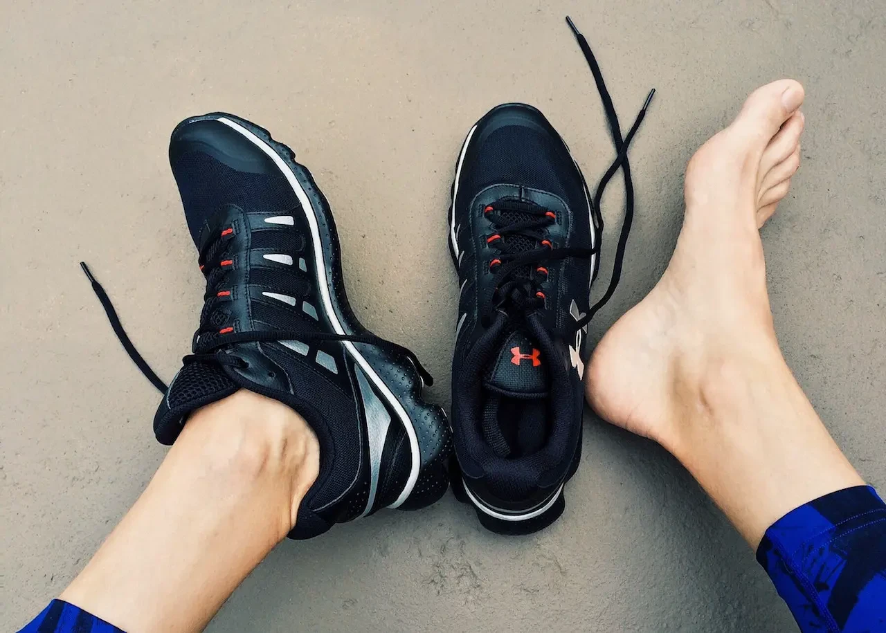 Bare foot beside running shoes showing common foot pain from athletic activity